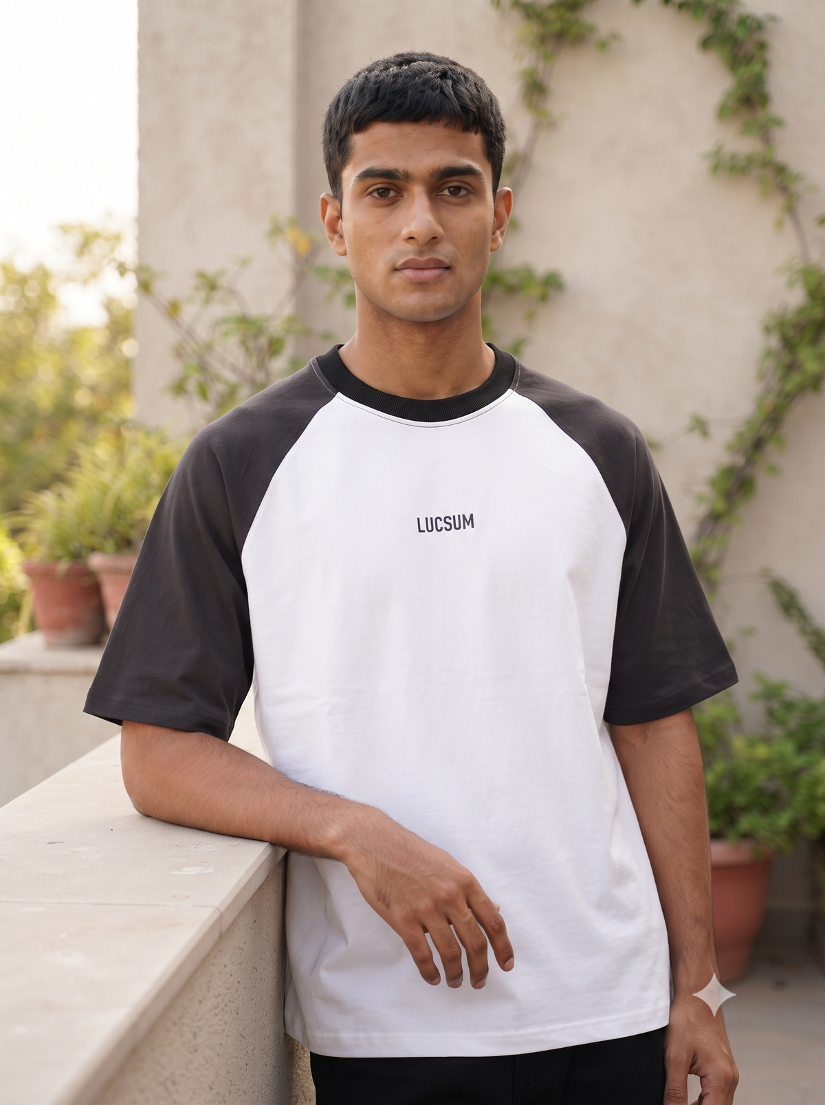 Lucsum Raglan white oversized tee with charcoal sleeves worn on a sunlit terrace, lifestyle portrait